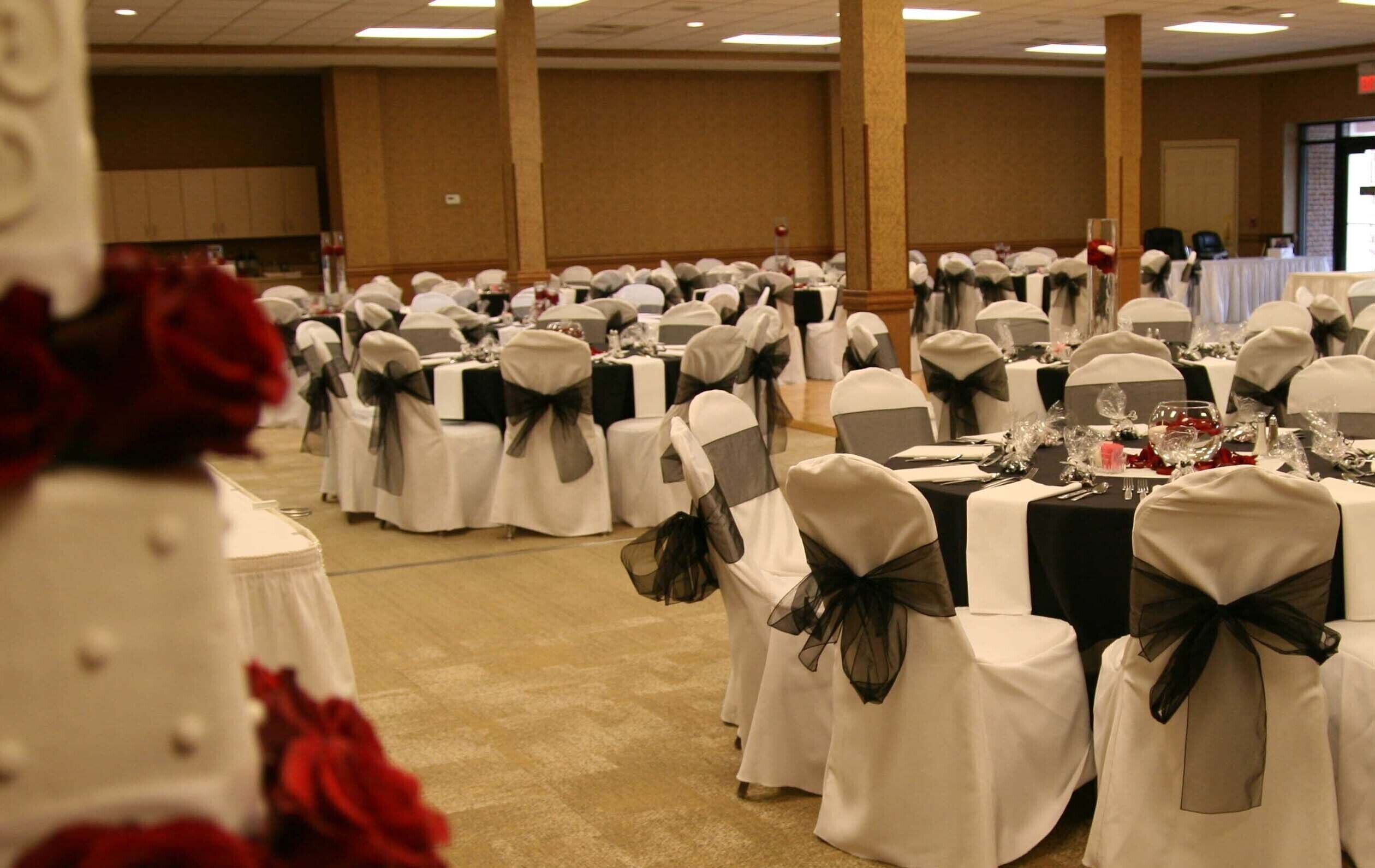 A banquet hall with rows of tables, each covered with white tablecloths and chairs adorned with black sashes.