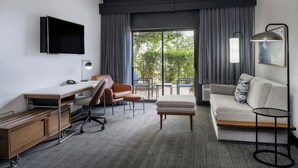 Ein modernes Hotelzimmer mit Flachbildfernseher, Schreibtisch mit Stuhl, Sofa, Pouf und Beistelltisch.