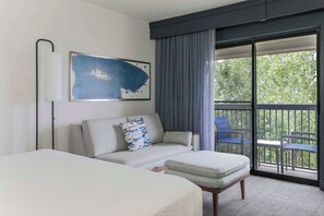 A hotel room with a bed, a sofa, a small table, a chair, and a balcony with a view of greenery. - Courtyard by Marriott Denver Golden/Red Rocks (Golden)