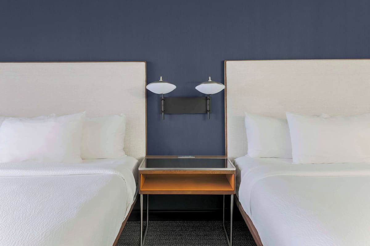 A hotel room with two beds, a small wooden table, and a wall-mounted TV.