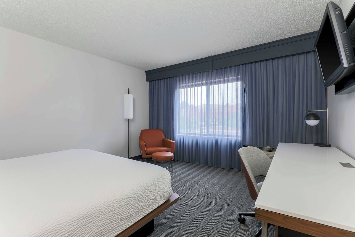 A hotel room with two beds, a desk, a chair, a TV, and a window with curtains.