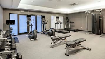 Un gimnasio moderno con cintas de correr, elípticas, bancos de pesas y una máquina de remo.