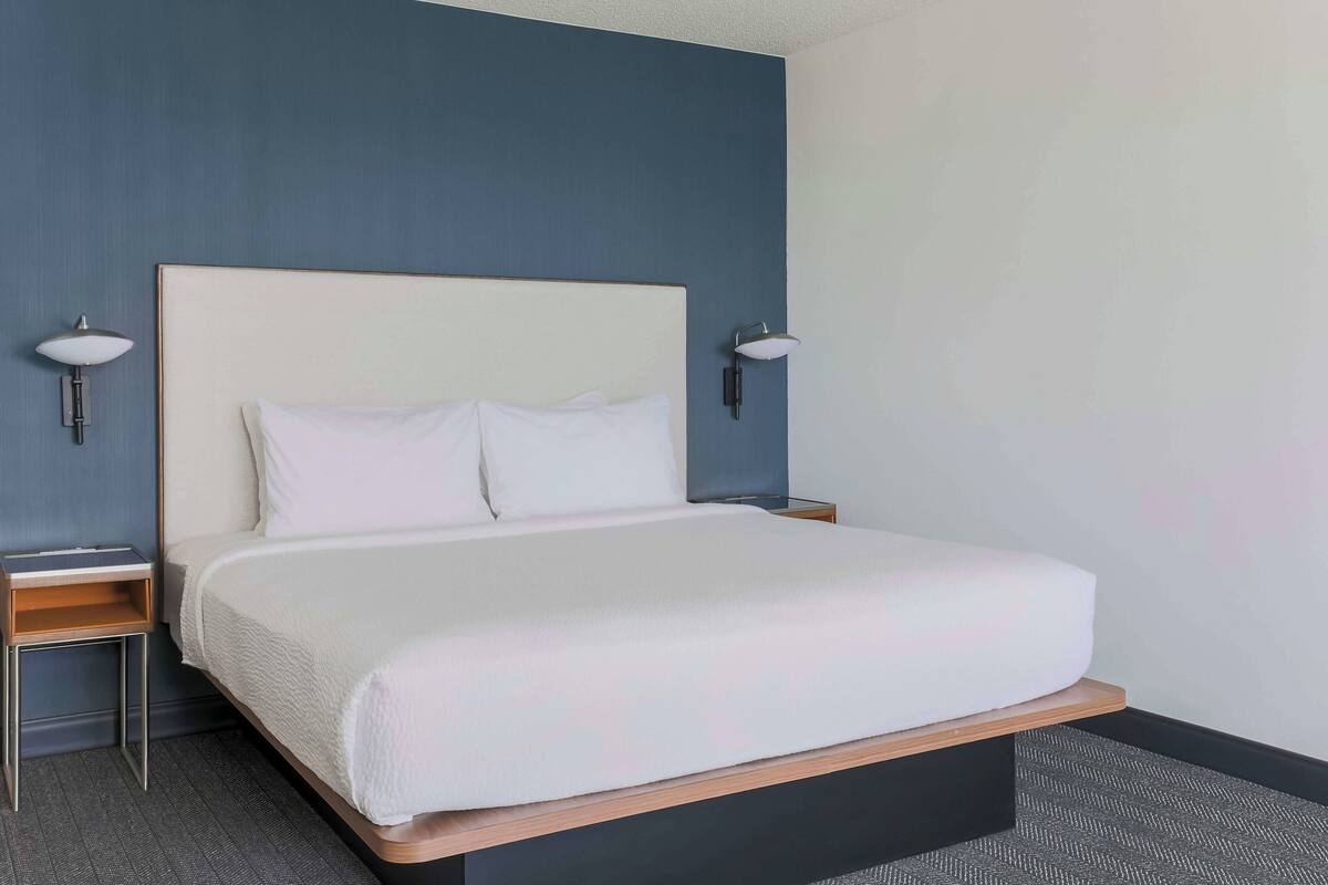 A hotel room with a large bed, two bedside tables, and wall-mounted lamps.