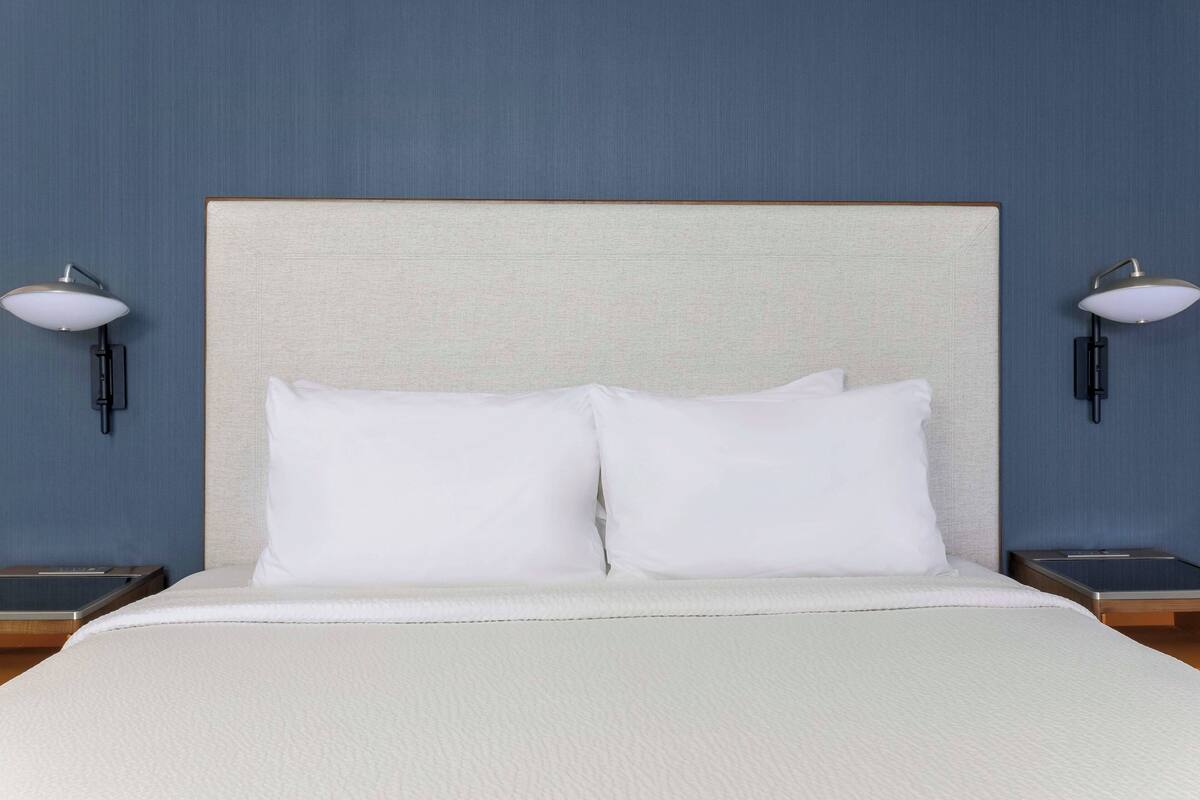 A hotel room with a large bed, two bedside tables, and two wall-mounted lamps.