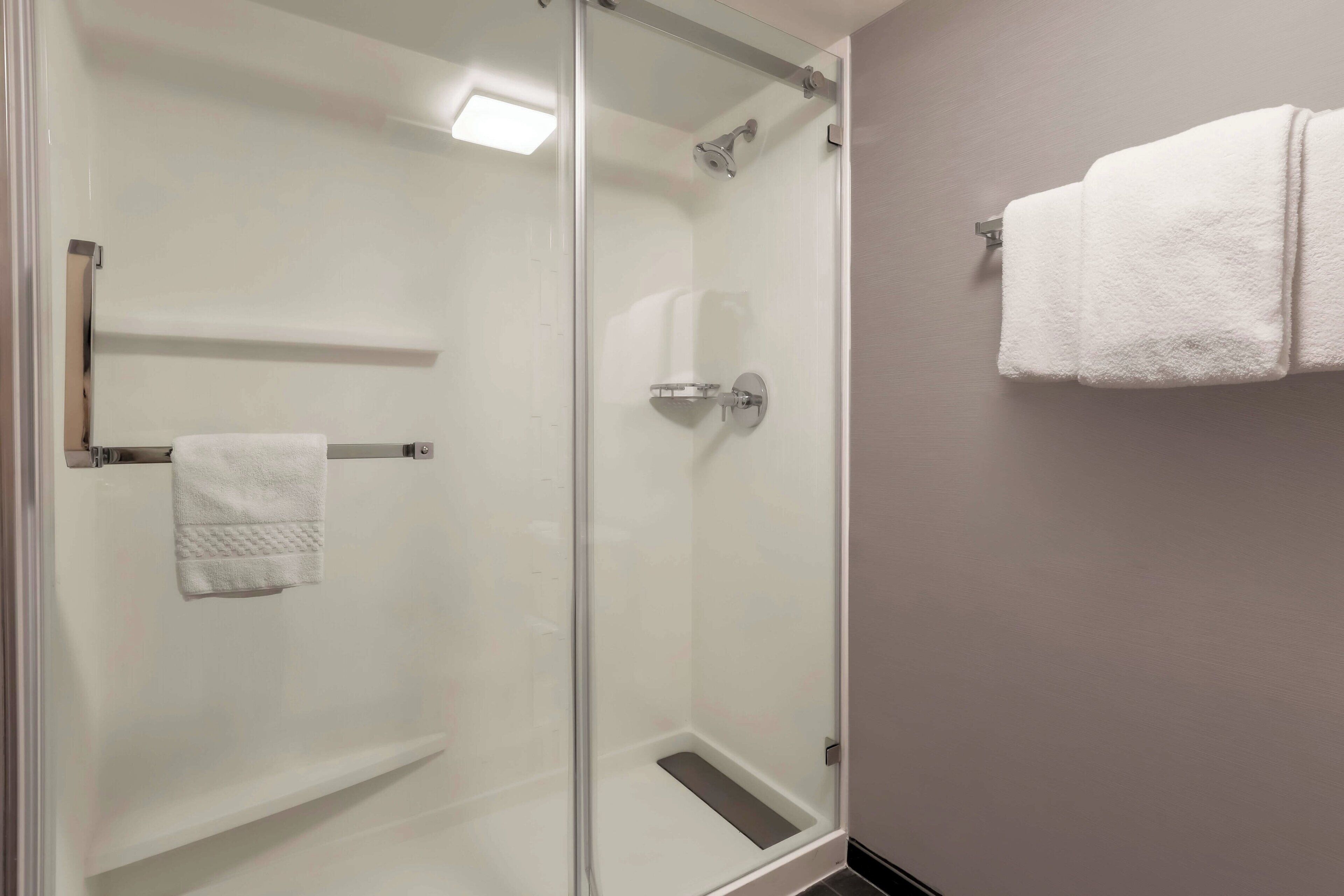 A glass-enclosed shower with a towel rack and a towel on the wall.
