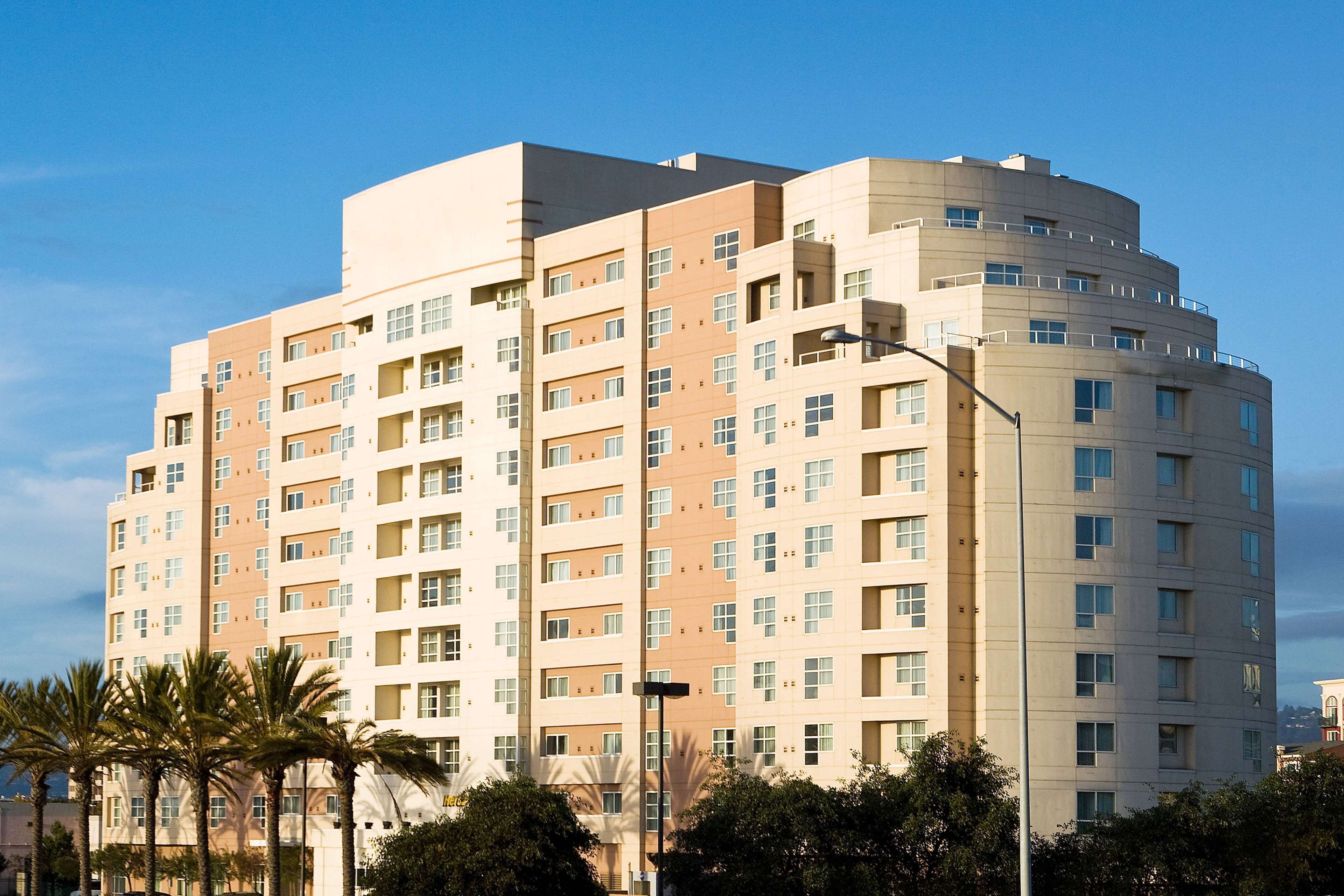 A multi-story hotel with a modern architectural design, featuring a series of balconies and a uniform facade.