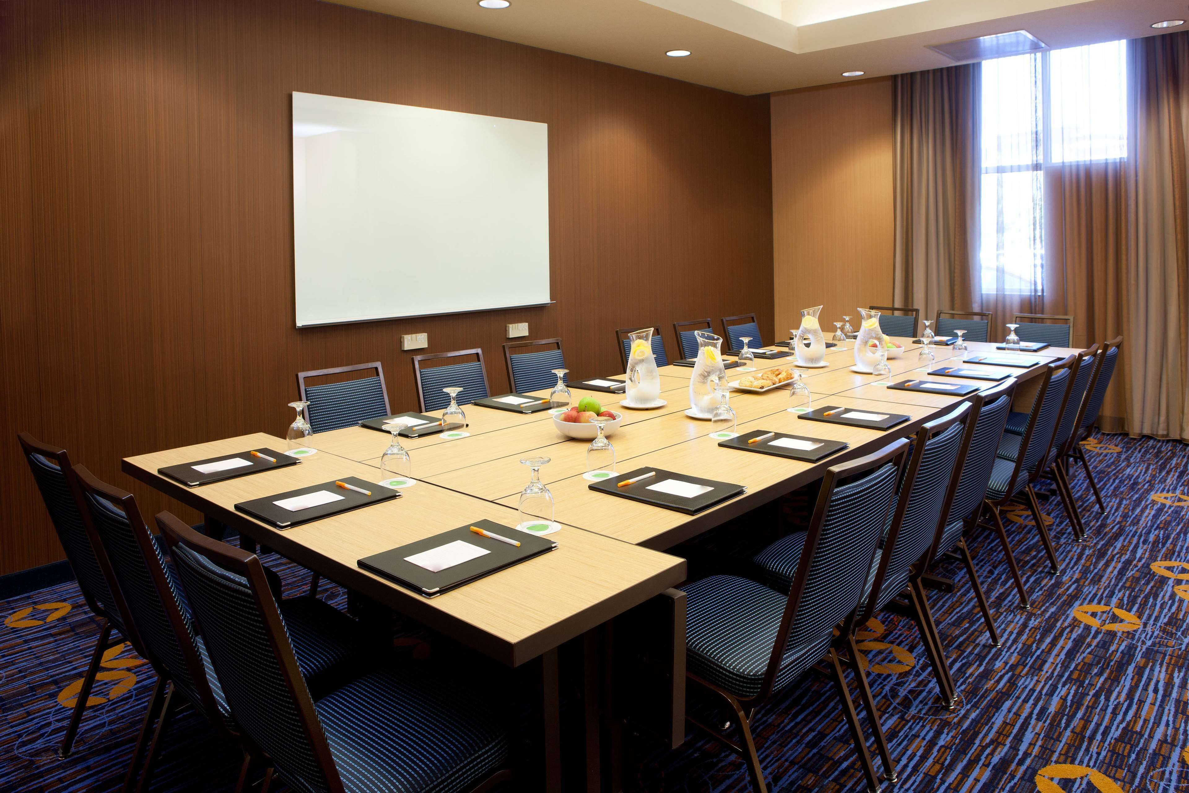 A conference room with a long table, chairs, a projector screen, and a window with curtains.