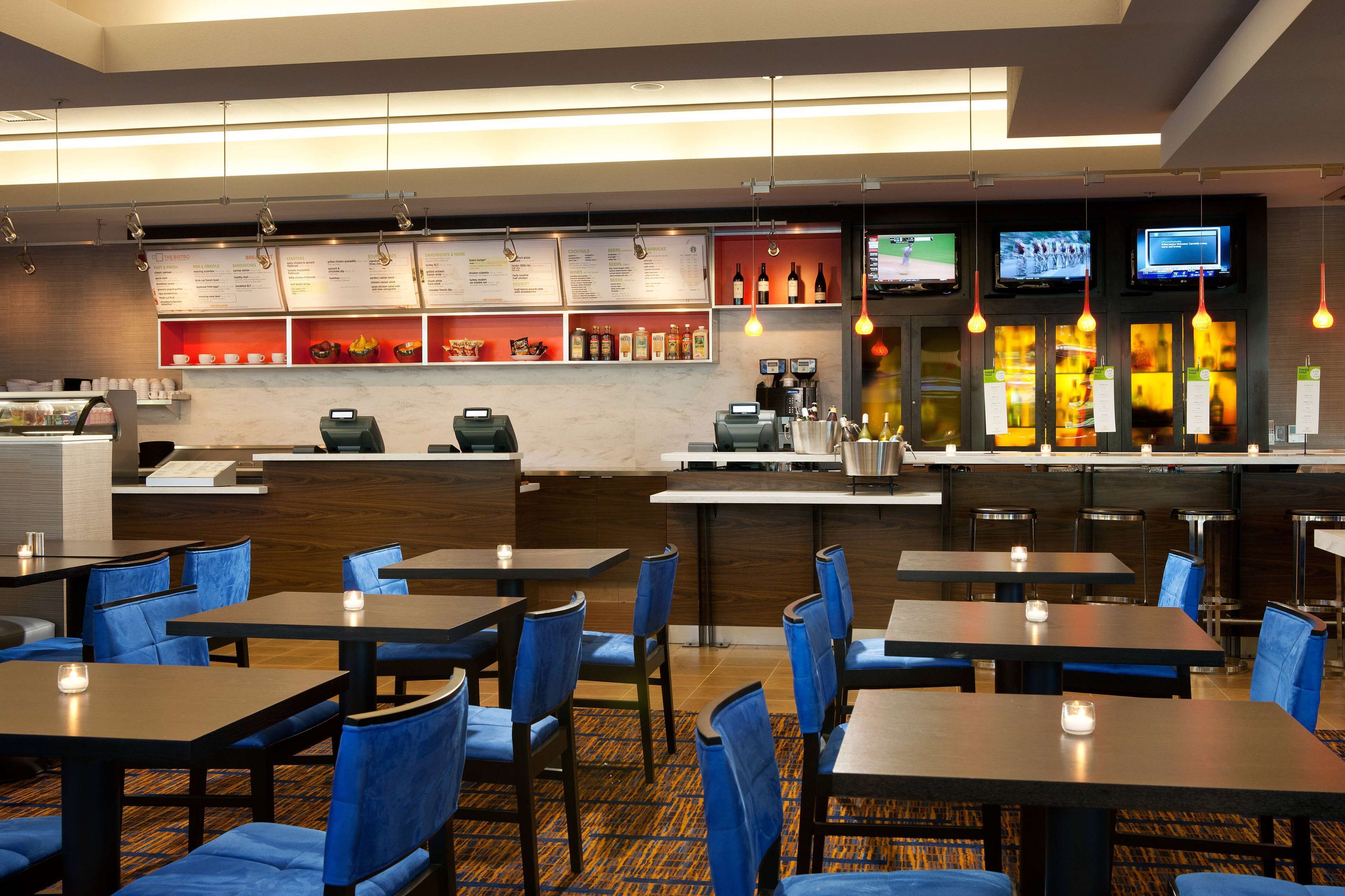 A hotel restaurant with tables and chairs, a counter with a menu, and a bar area with bottles.