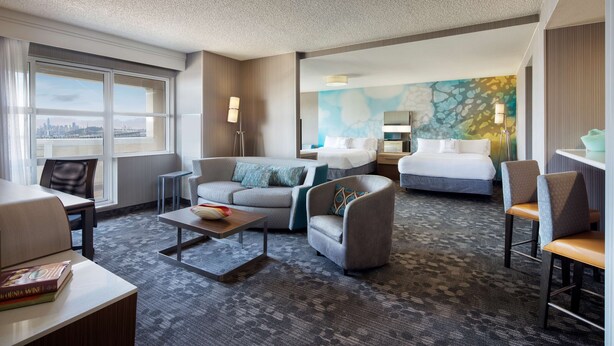 Een hotelkamer met een bank, fauteuil en een bed. Er is uitzicht op de stad vanuit het raam.