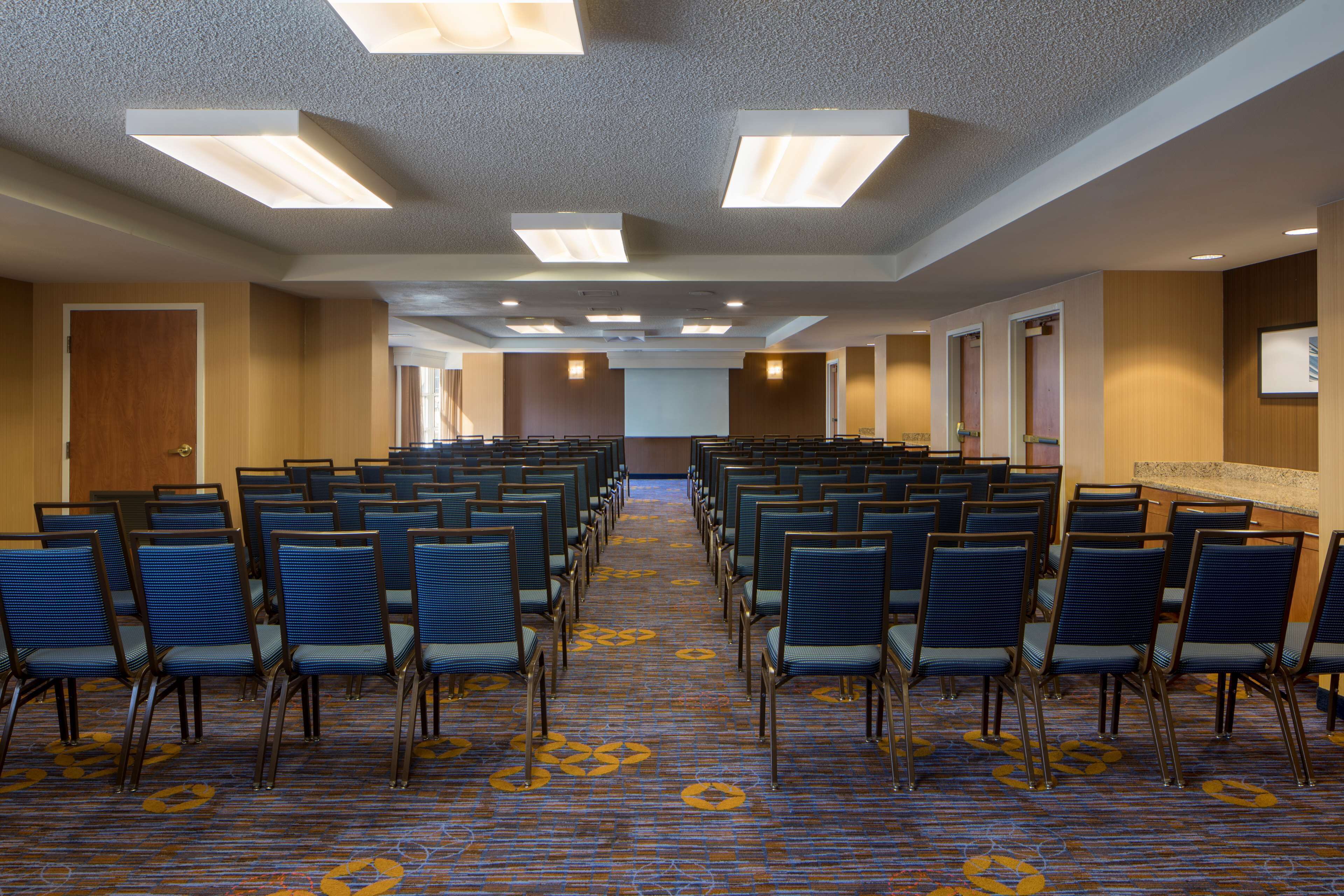 A conference room with rows of chairs, a patterned carpet, and ceiling lights.