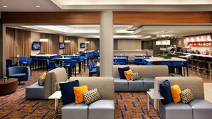 Een moderne hotel lobby met zithoeken, een bar en een televisiescherm.