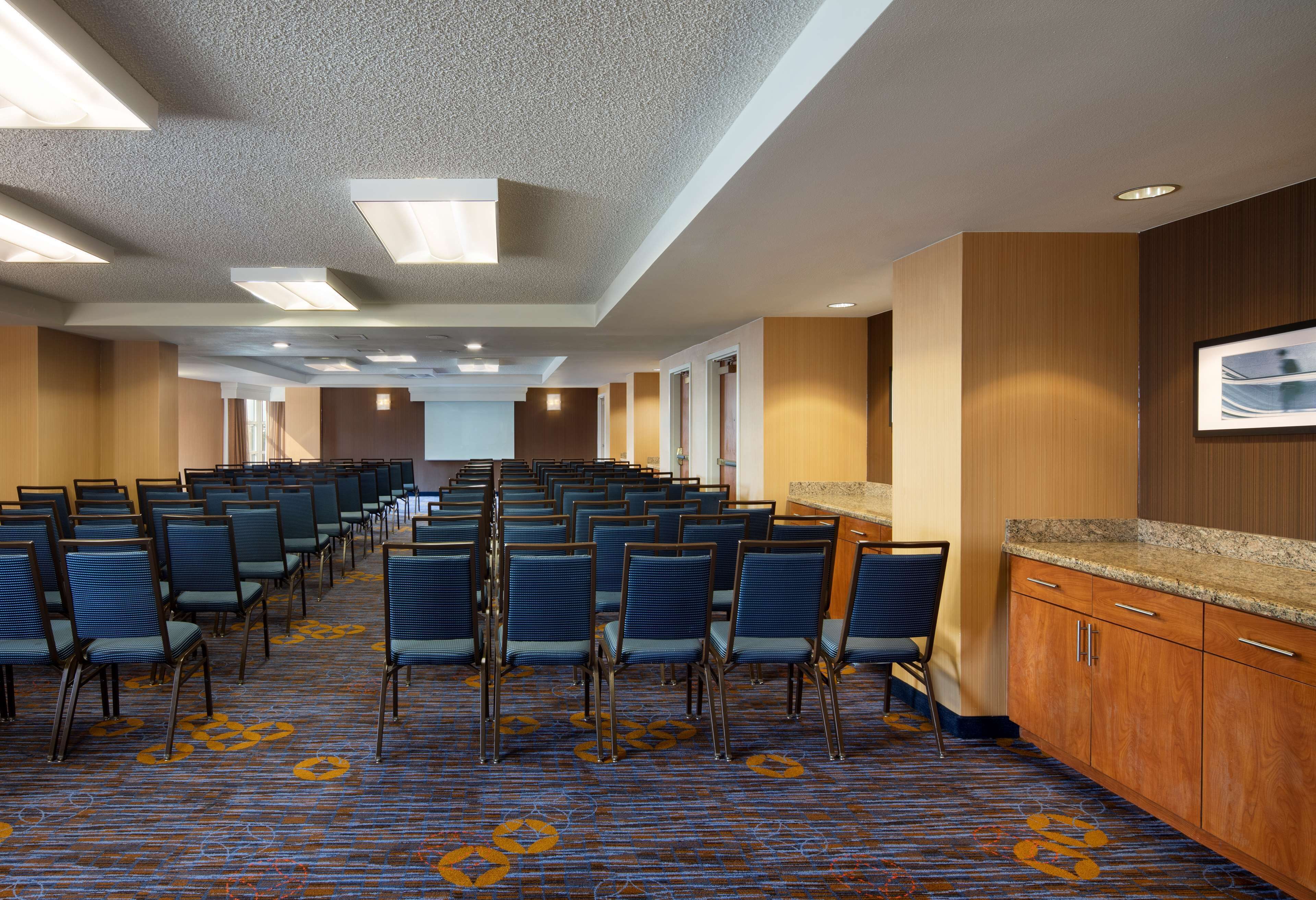 Un salón de conferencias con filas de sillas, suelo alfombrado, paneles de madera y un mostrador con cajones.