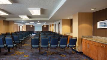 Un salón de conferencias con filas de sillas, suelo alfombrado, paneles de madera y un mostrador con cajones.