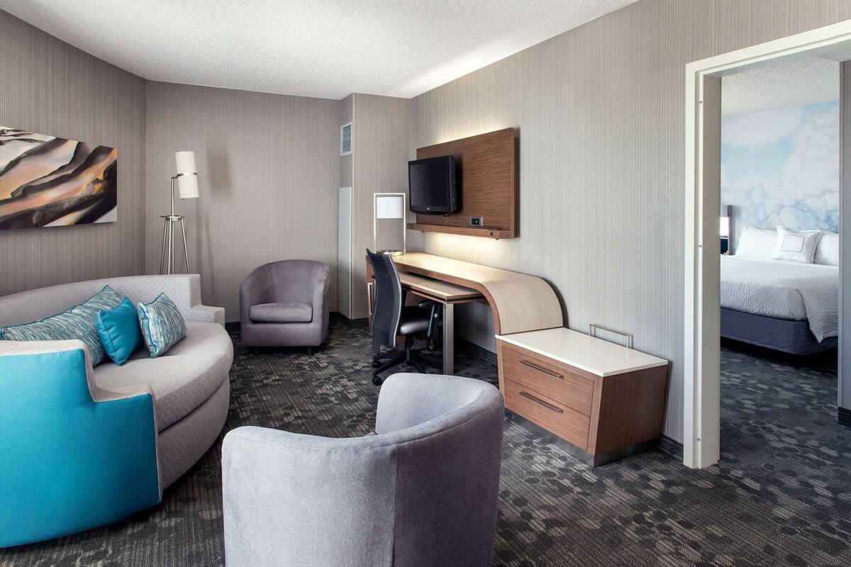 Een hotelkamer met een gebogen bank, een bureau, een stoel, een bed en een aan de muur bevestigde televisie.
