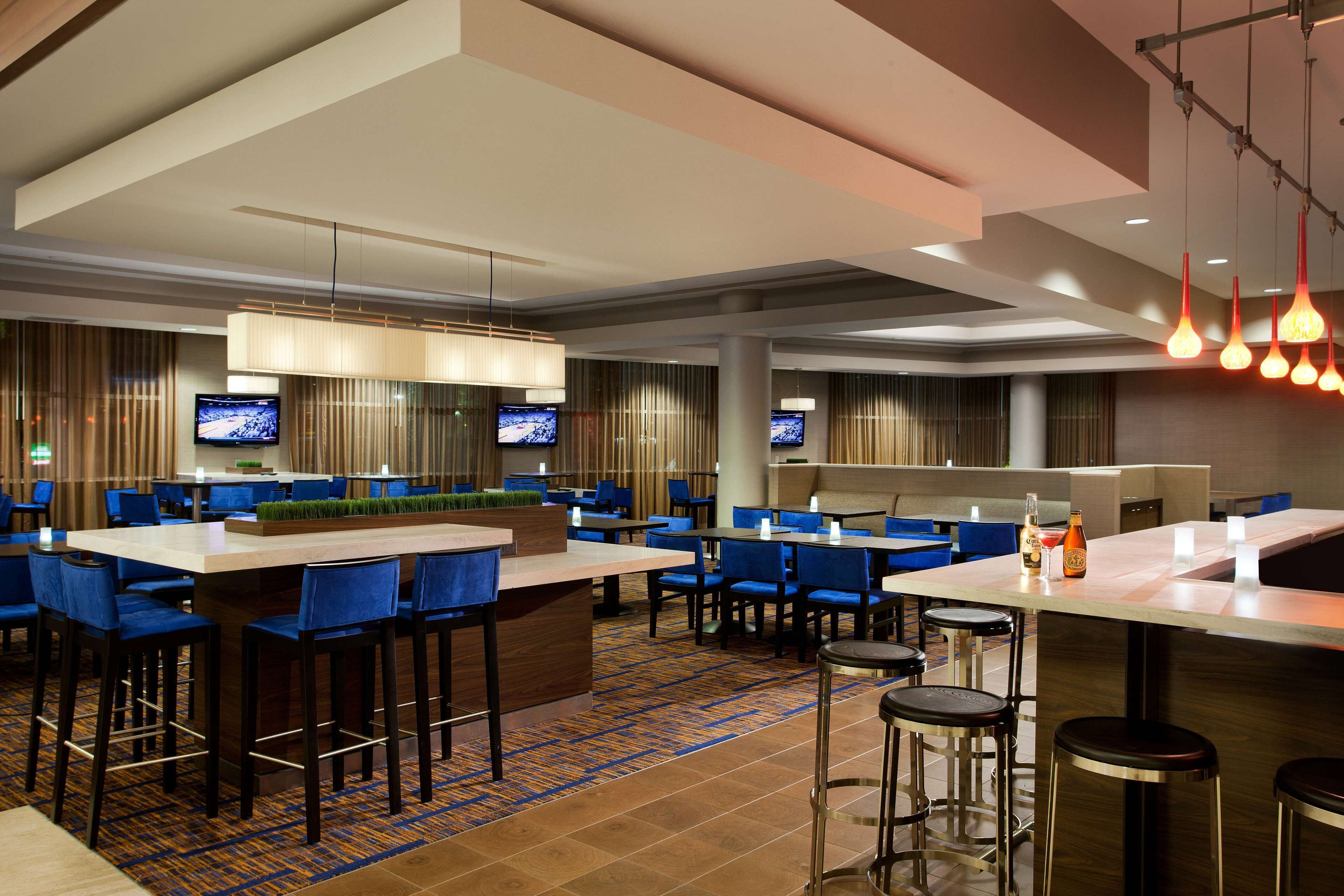 Un moderno vestíbulo de hotel con varias zonas de estar, taburetes de bar y una barra central.