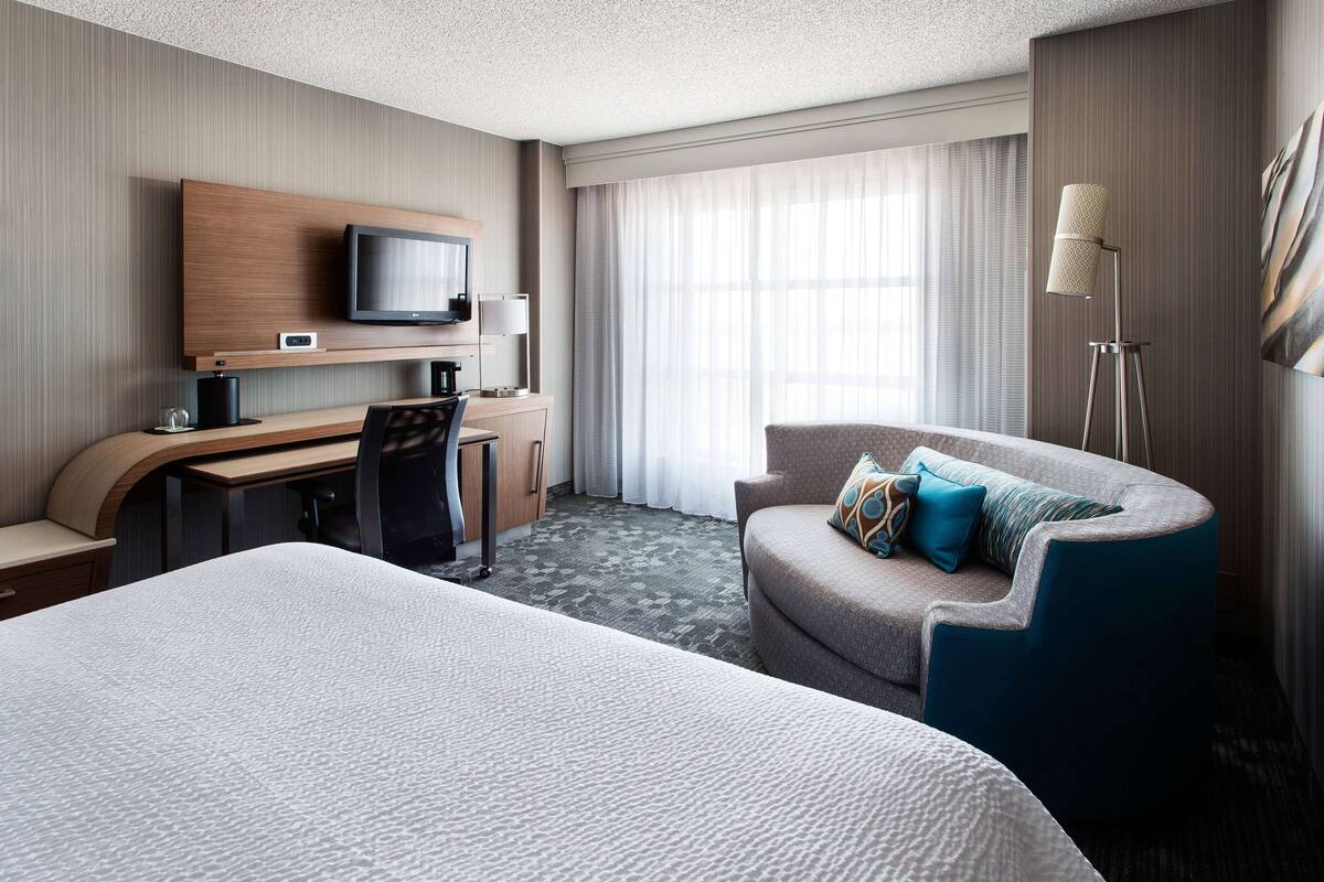 Een hotelkamer met een groot bed, een bureau met een computer, een stoel, een aan de muur bevestigde televisie en een vloerlamp.