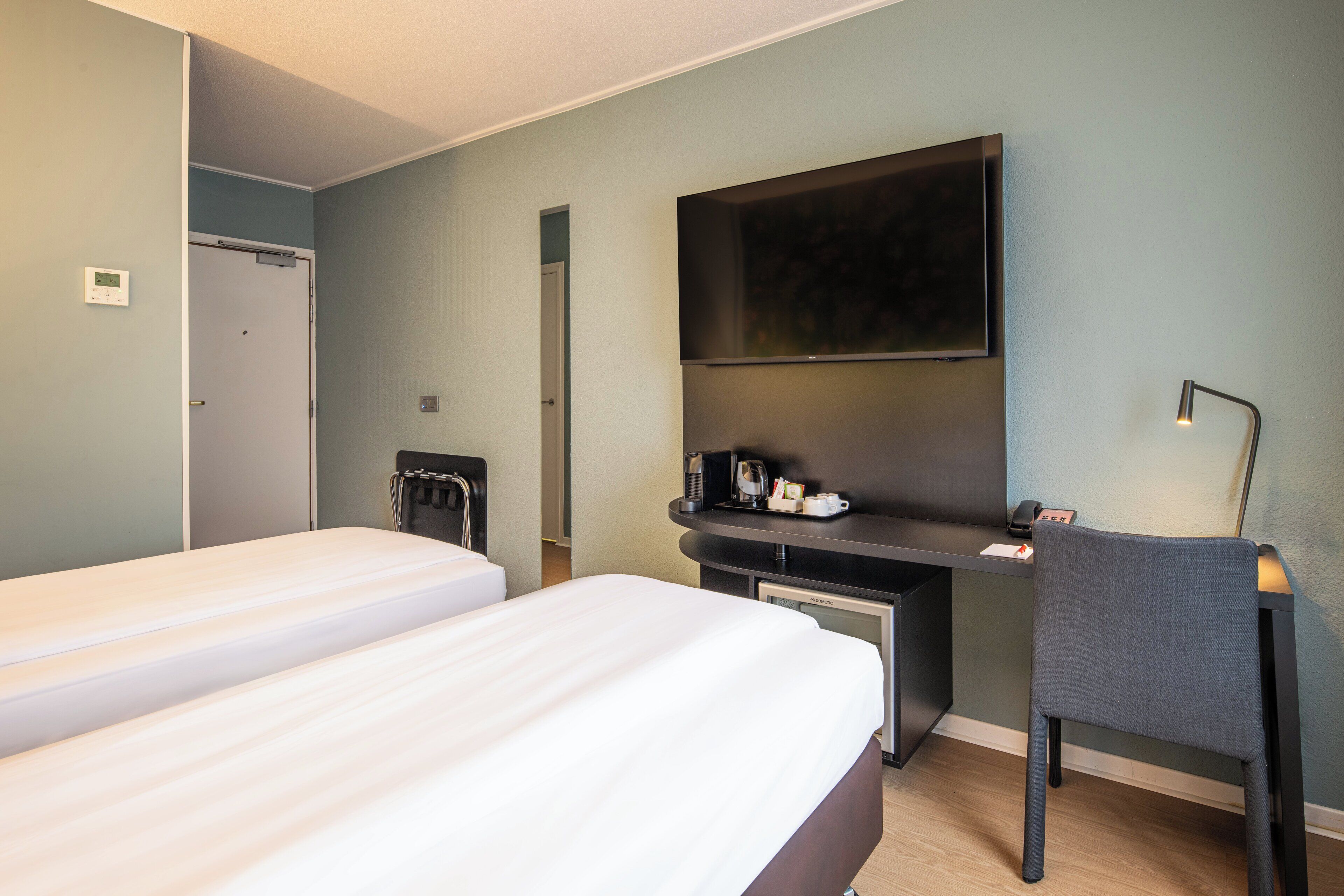 A hotel room with two beds, a desk with a chair, a flat-screen TV, a coffee maker, and a desk lamp.