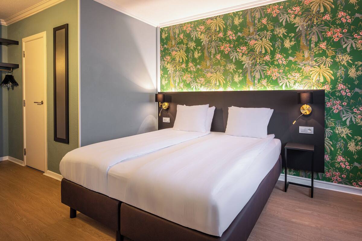 Een opgemaakt bed met witte lakens, een donker hoofdbord en twee bedlampjes.