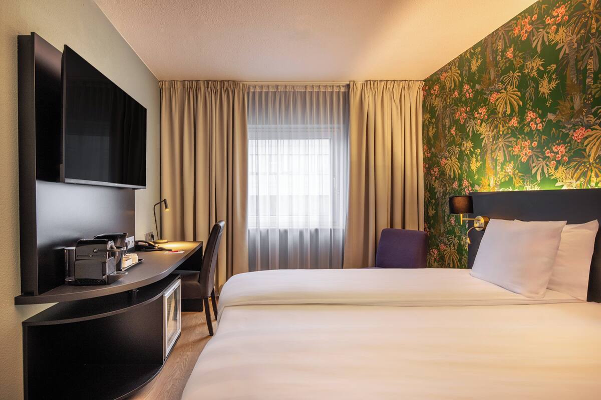 Een hotelkamer met een bed, een bureau met een computer, een televisie en een raam met gordijnen.