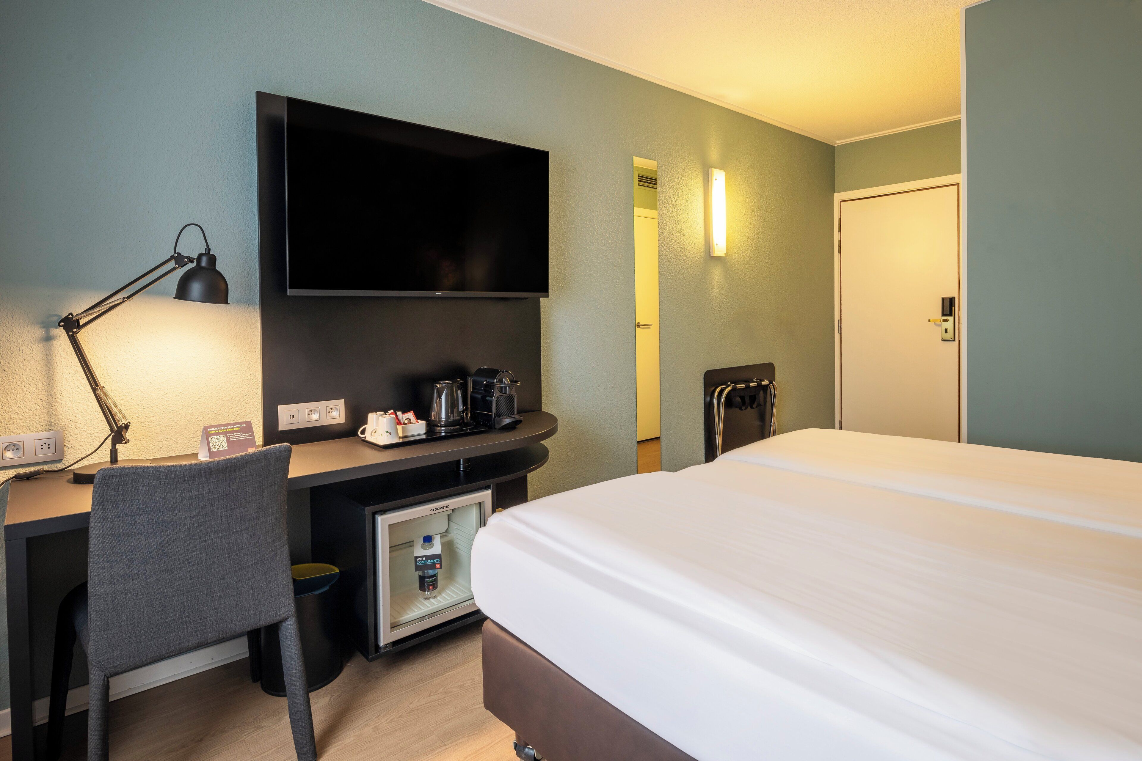 Ein Hotelzimmer mit Bett, Schreibtisch, Fernseher und einer Minibar.