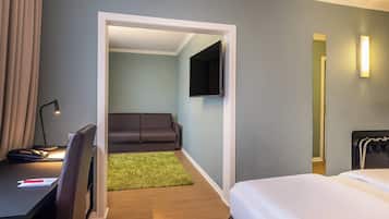 Et hotelværelse med en seng, et skrivebord med stol, en sofa, et grønt tæppe og et fjernsyn ophængt på væggen.