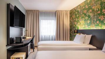 A hotel room with two beds, a desk with a flat-screen TV, a minibar, and a large window with curtains.