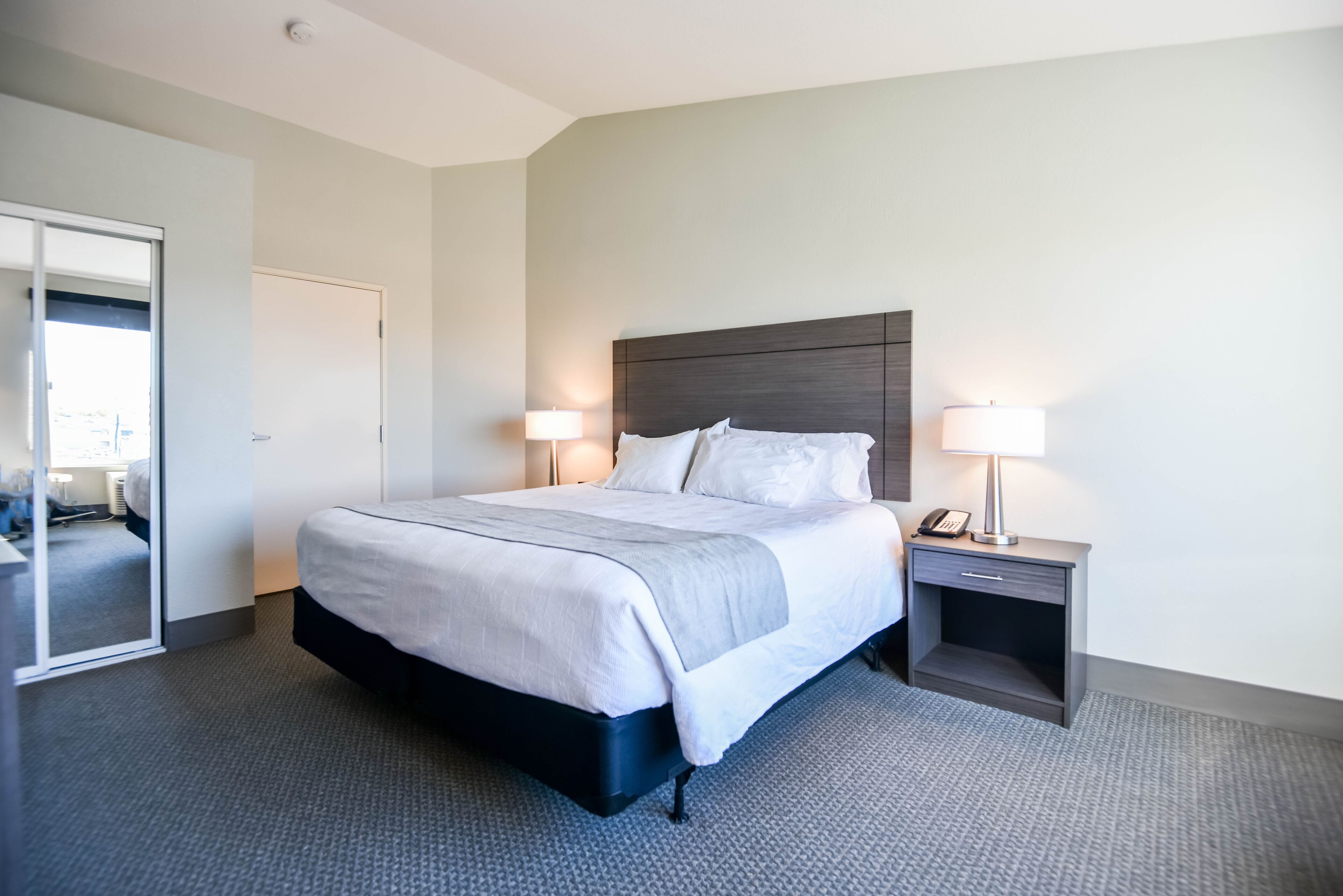 A modern hotel room with a large bed, bedside lamps, a nightstand, and a mirror.