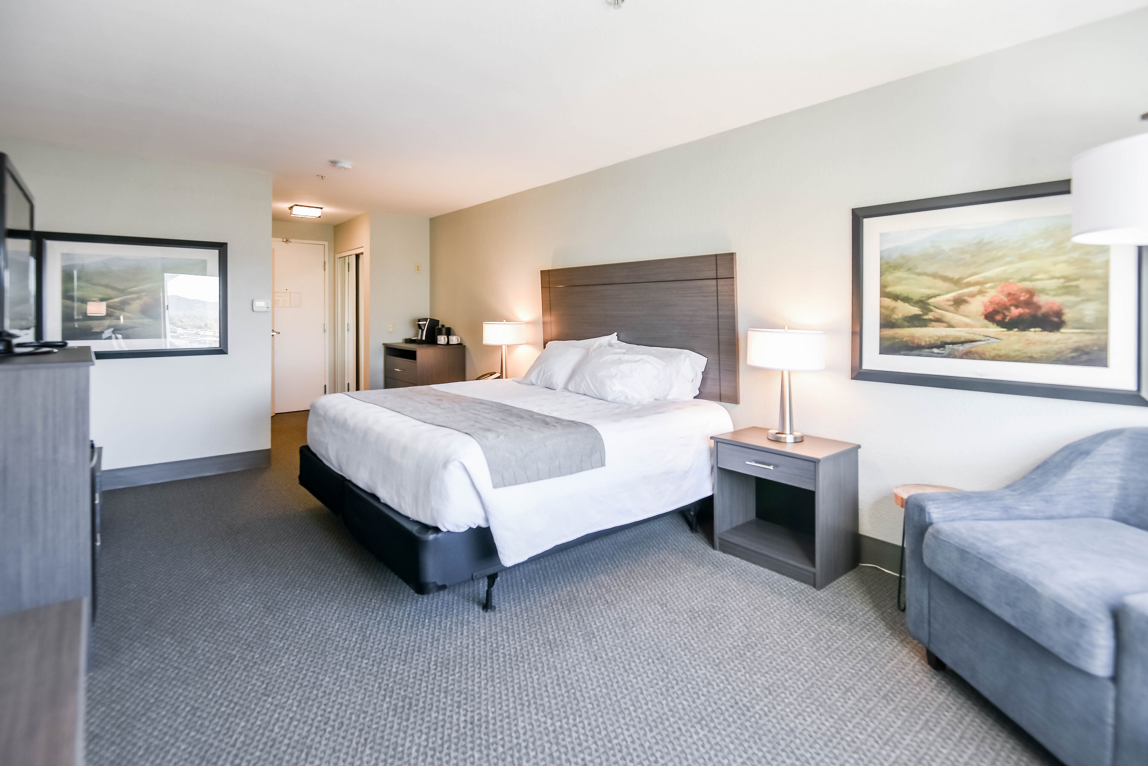 A hotel room with a large bed, bedside tables, a desk, a chair, and a framed picture on the wall.