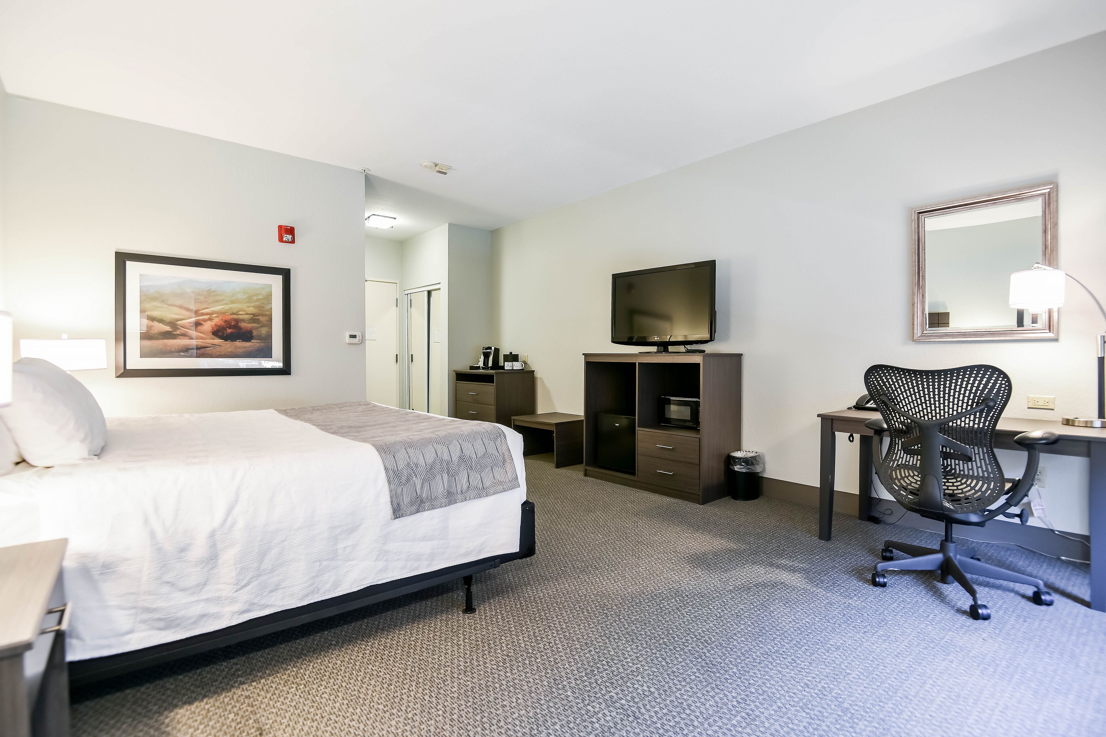 Een hotelkamer met een bed, bureau, stoel, televisie en een ingelijst schilderij aan de muur.