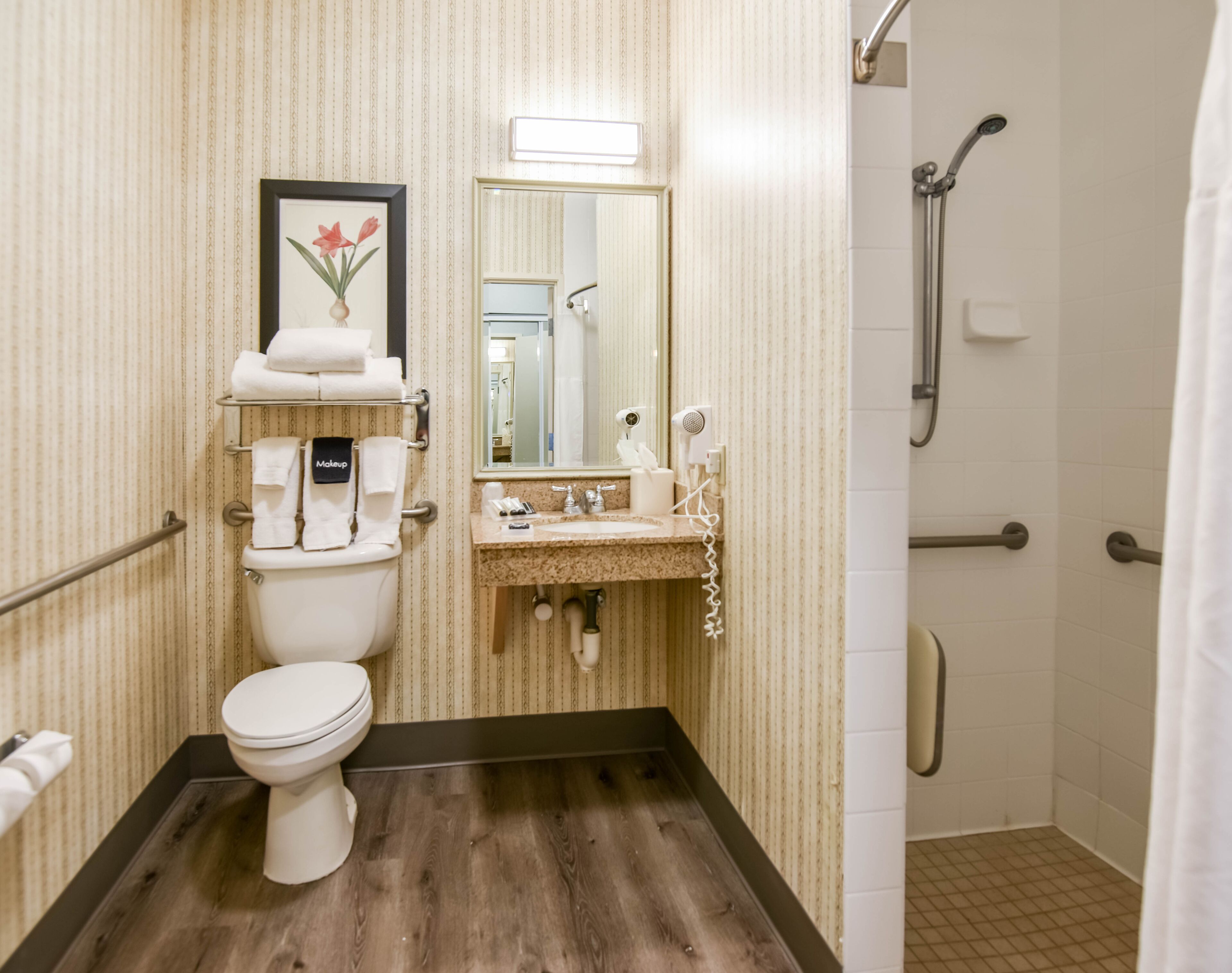 A bathroom with a toilet, sink, and shower. There is a framed picture on the wall, and towels are neatly arranged on a rack.
