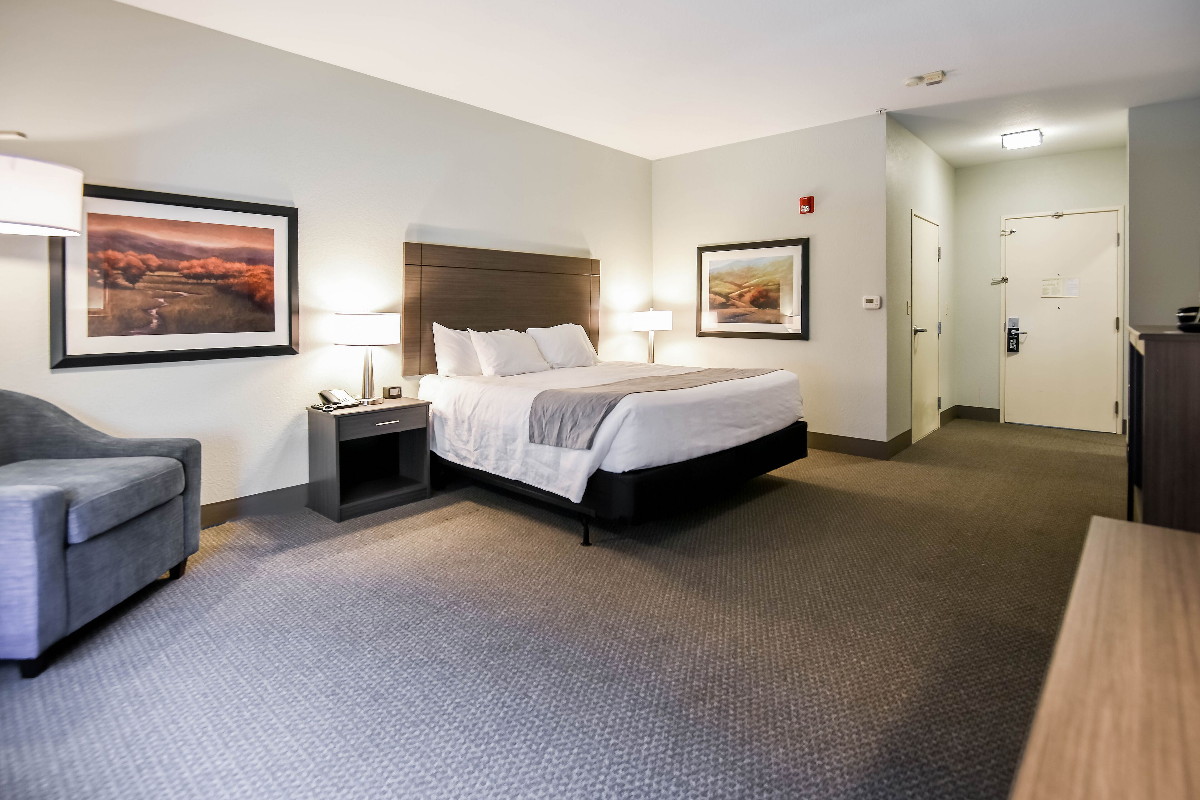 Habitación de hotel con una cama, un escritorio, una silla y dos cuadros en las paredes.