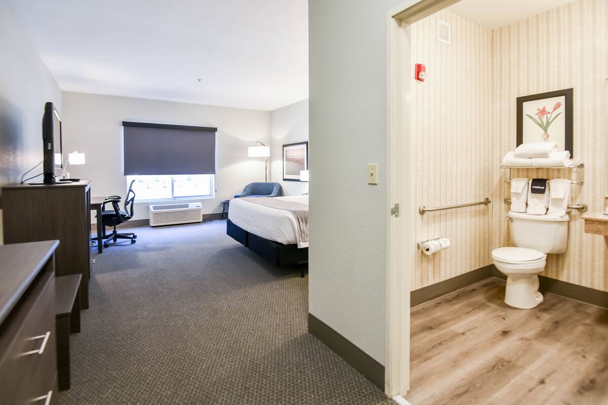 A hotel room with a desk, chair, bed, and a view of the city.