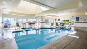 Una piscina interior con paredes de vidrio transparente, múltiples sillones de descanso y suelo de baldosas.