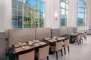 A modern dining area with high windows, cushioned seating, and neatly arranged tables. - Hilton Garden Inn Charlotte Uptown (Charlotte)