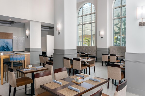 A modern dining area with high ceilings, large windows, and contemporary furniture. - Hilton Garden Inn Charlotte Uptown (Charlotte)