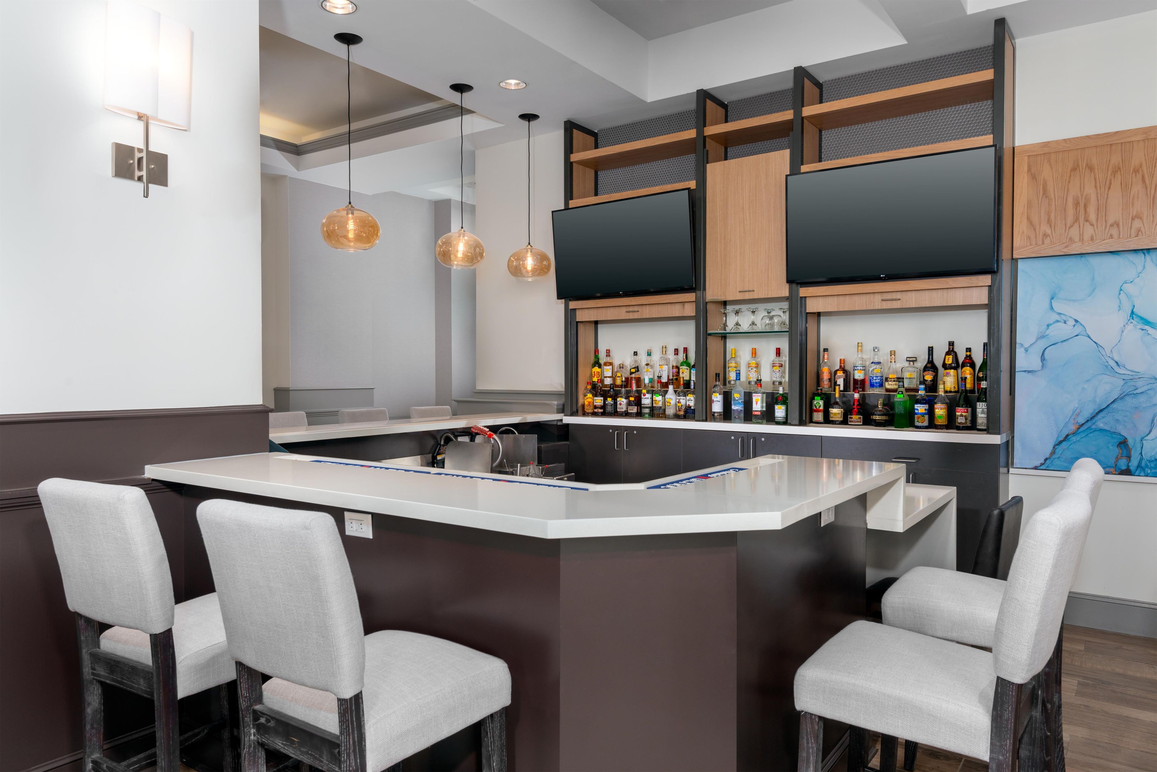 Un espace bar moderne doté d’un îlot central, de tabourets de bar, de luminaires suspendus et d’une variété de bouteilles d’alcool.