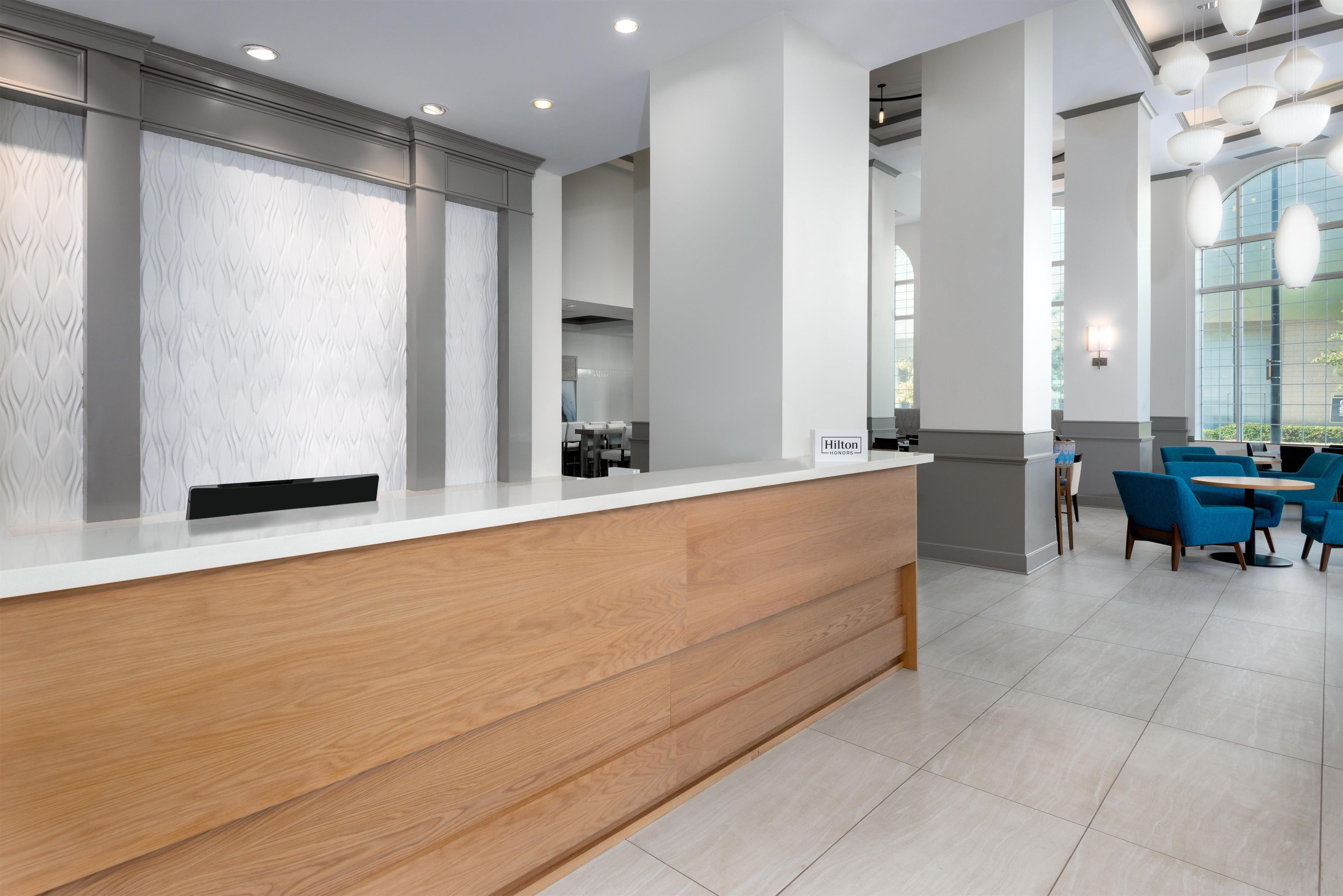 A reception desk with a wooden finish, a seating area with blue chairs, and a large window providing natural light.