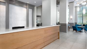 A reception desk with a wooden finish, a seating area with blue chairs, and a large window providing natural light.