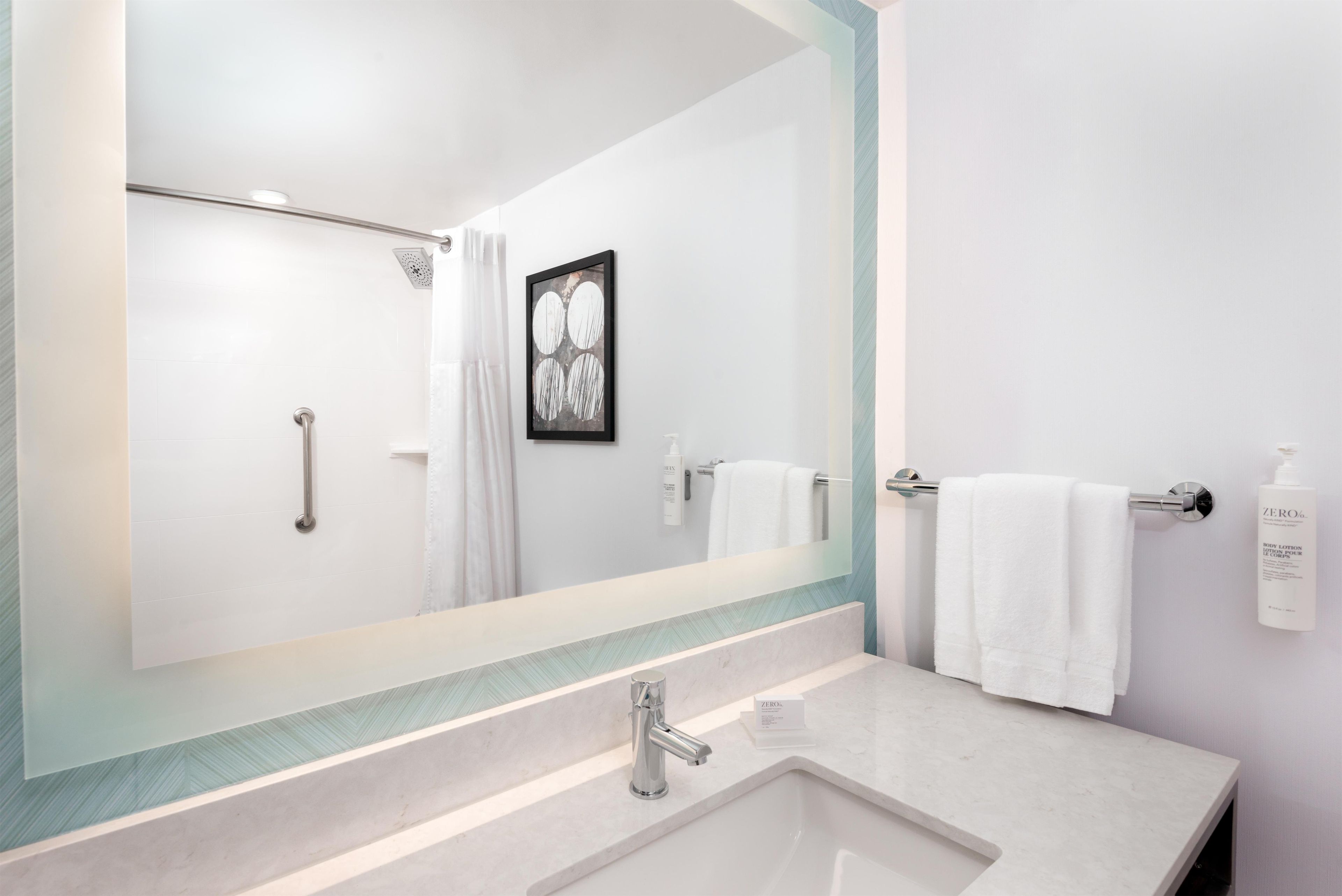 A modern bathroom with a large mirror, a shower with a handheld showerhead, a sink with a faucet, and a towel rack with two white towels.