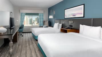 A hotel room with two beds, a desk, a chair, a TV, and a window with curtains.