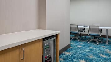 A conference room with a white table, four chairs, and a refrigerator with beverages.