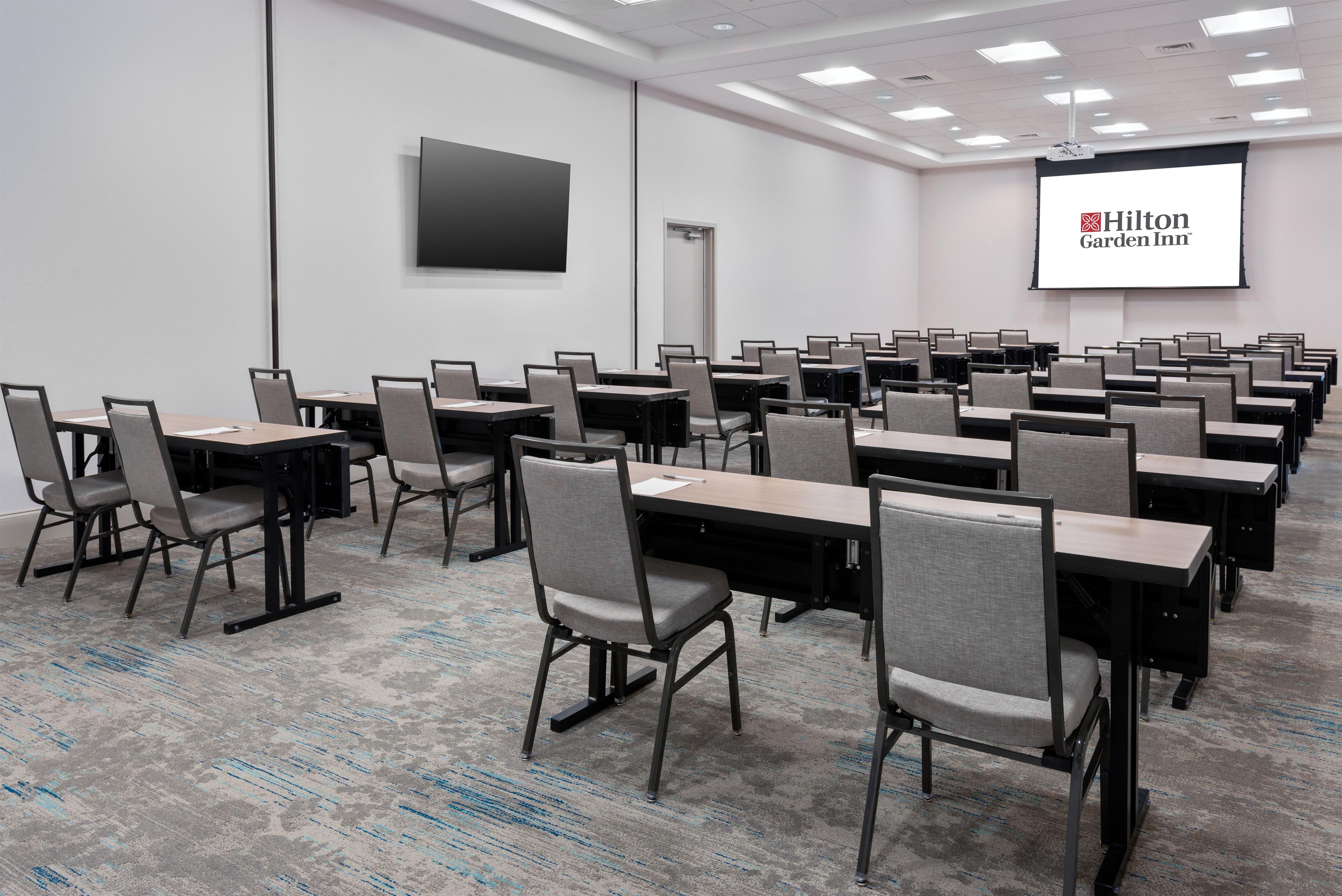 A conference room with rows of tables and chairs, a projector screen, and a door.