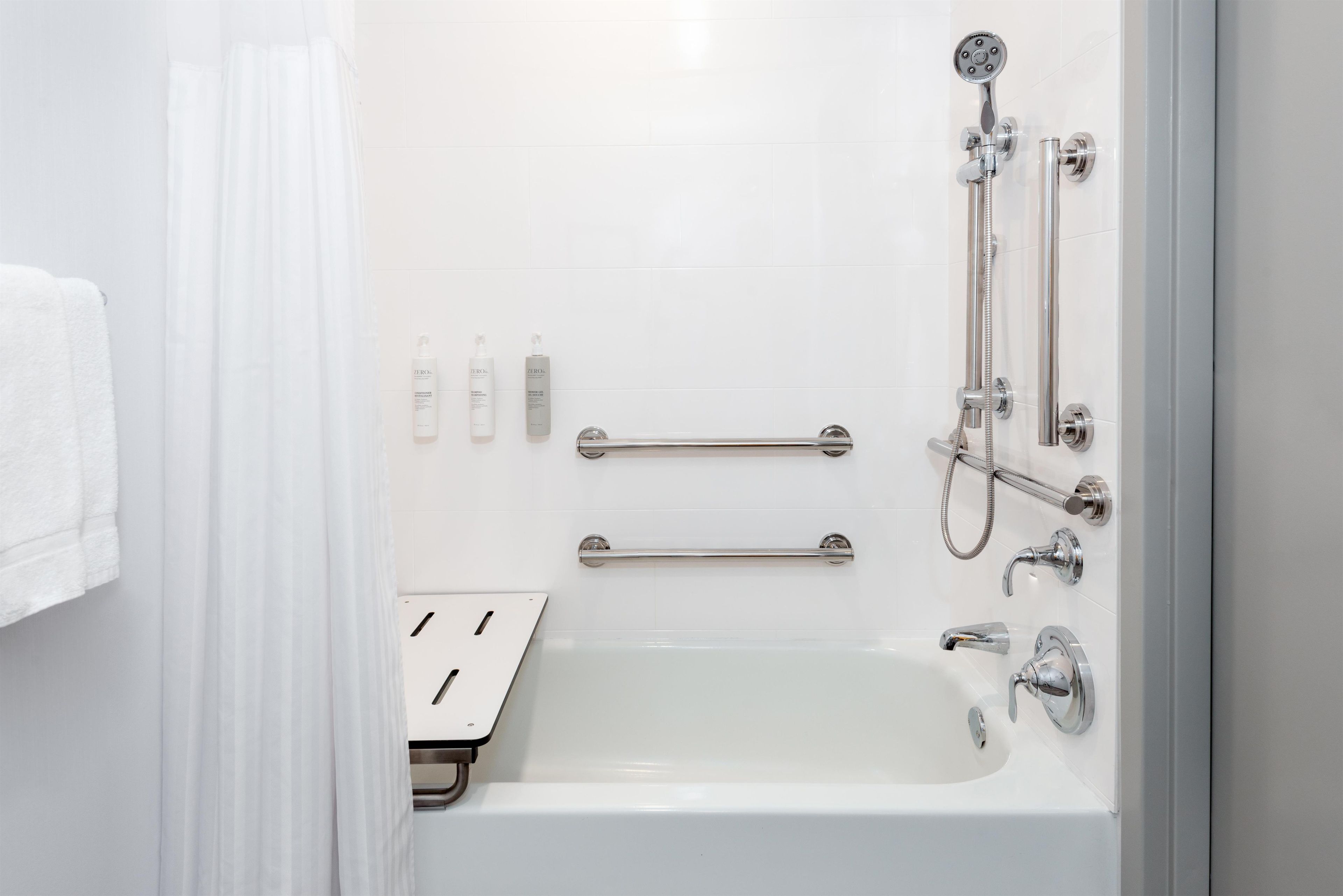 A modern bathroom with a bathtub, shower, and handrails.