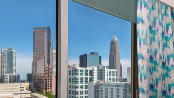 A cityscape through a window with modern buildings, a clear sky, and a patterned curtain.