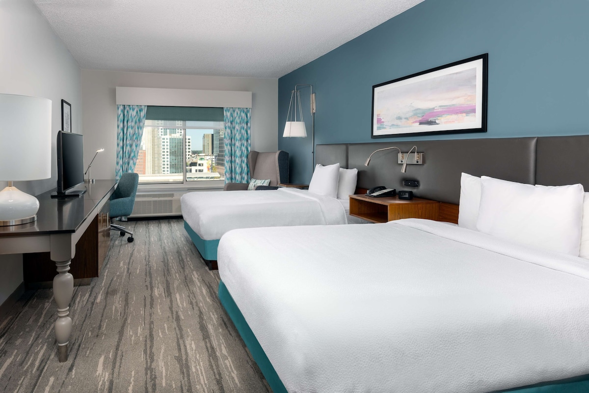 A hotel room with two beds, a desk, a chair, a TV, and a window with curtains.