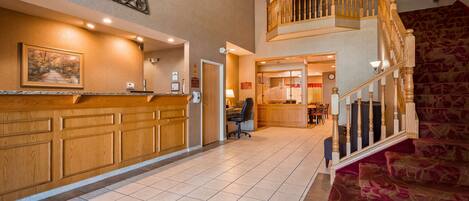 A hotel lobby with a reception desk, a staircase, and a dining area.
