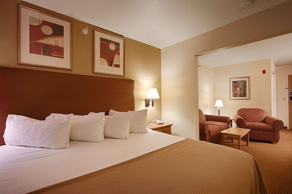 Una habitación de hotel con una cama grande, dos sillas, una mesita de noche y una puerta.