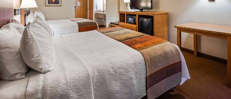 A hotel room with two beds, a TV, a desk, and a bathroom visible through an open door.