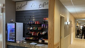 A corridor with a snack bar named "Refuel & Lift" featuring a refrigerator stocked with cold drinks and shelves with snacks and packaged goods.