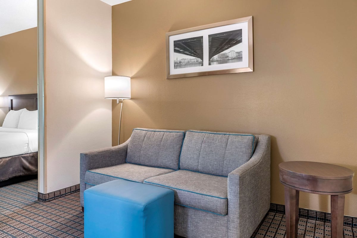 A hotel room with a gray sofa, a blue ottoman, a small round table, and a framed picture on the wall.